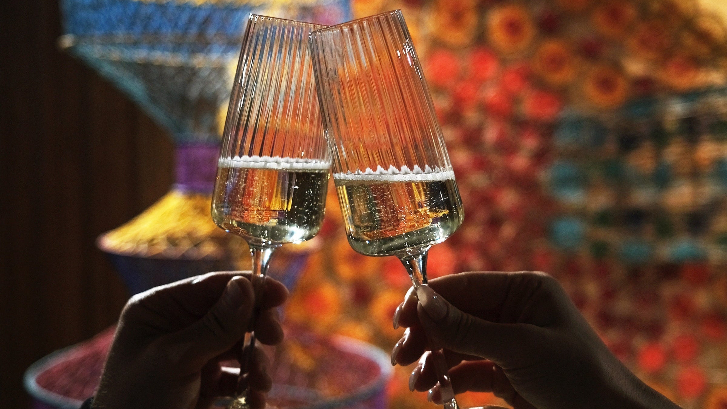 Two hands hold Exclusiva Flute glasses with wine cheering