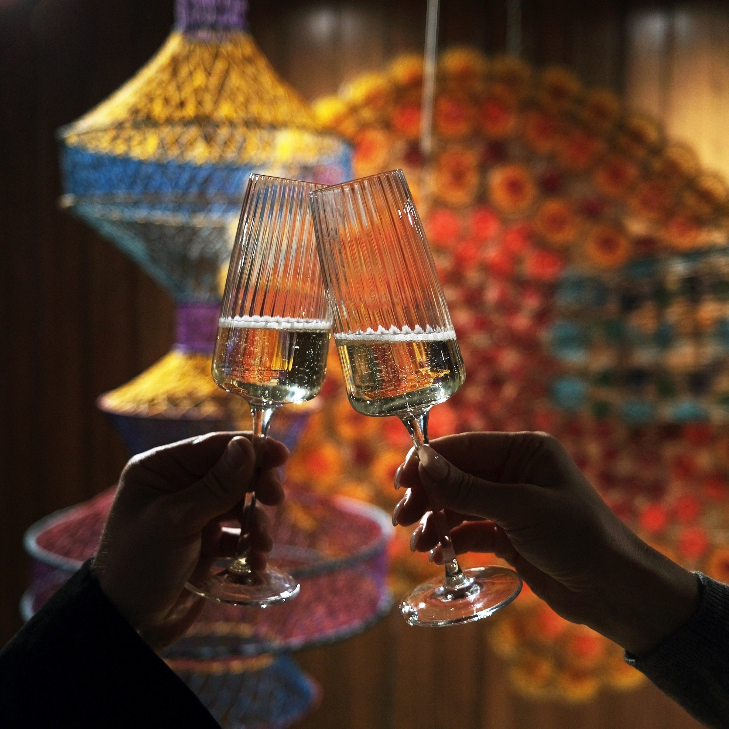 Two hands hold Exclusiva Flute glasses with wine cheering