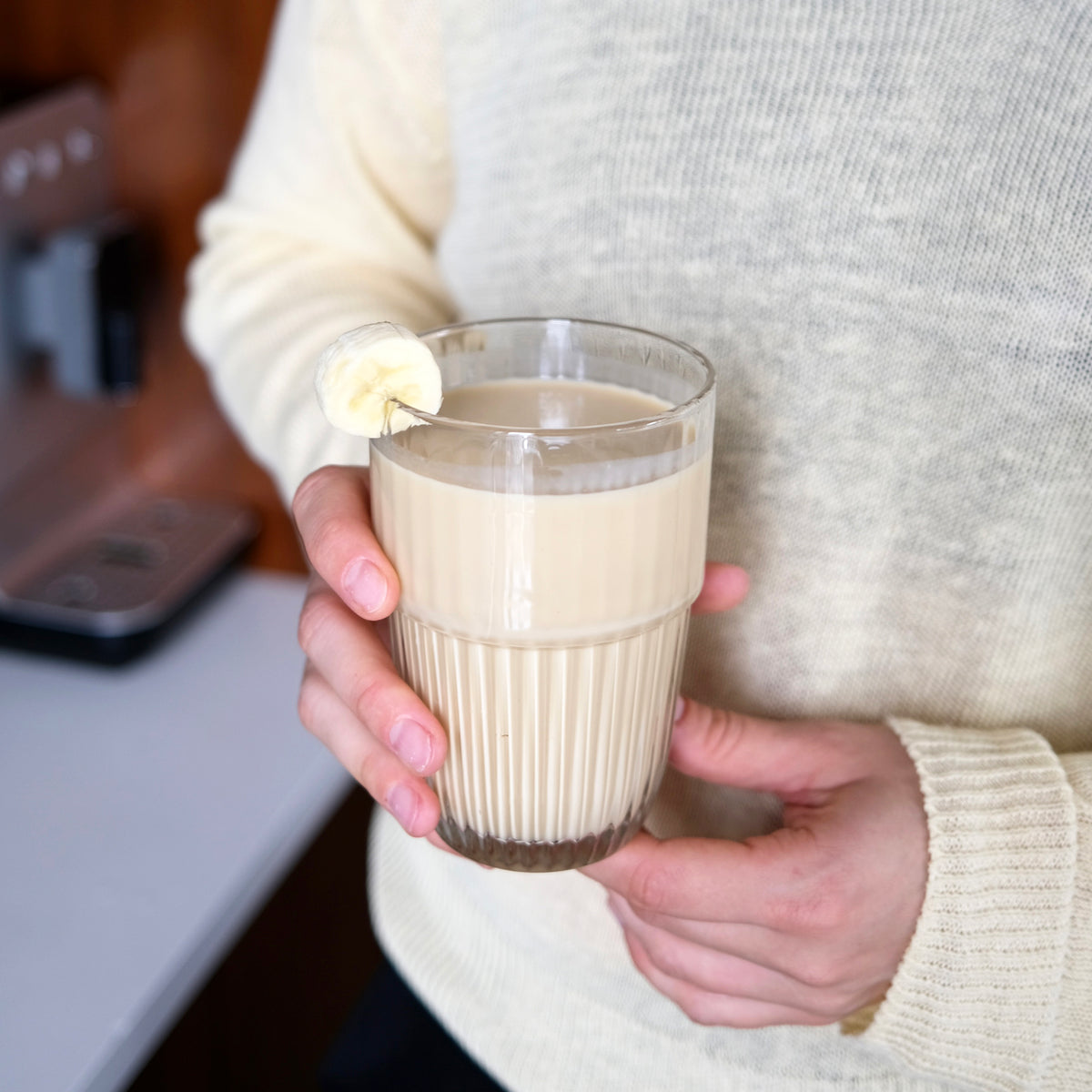 Person holding a glass of creamy beverage with a kitchen background