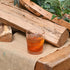 Novecento DOF glass with amber liquid on a rustic wooden surface with plants in the background