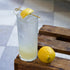 Exclusiva Tom Collins glass filled with a light cocktail with lemon garnish on a wooden crate with a lemon next to it