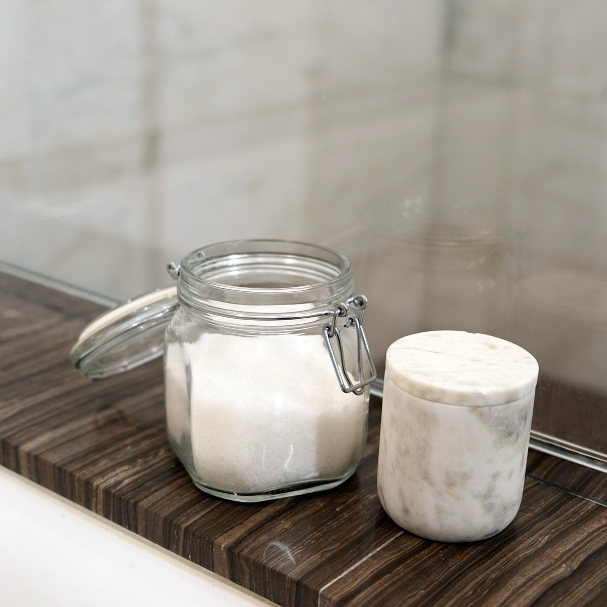 Glass jar with a marble lid on a wooden surface next to a marble container.