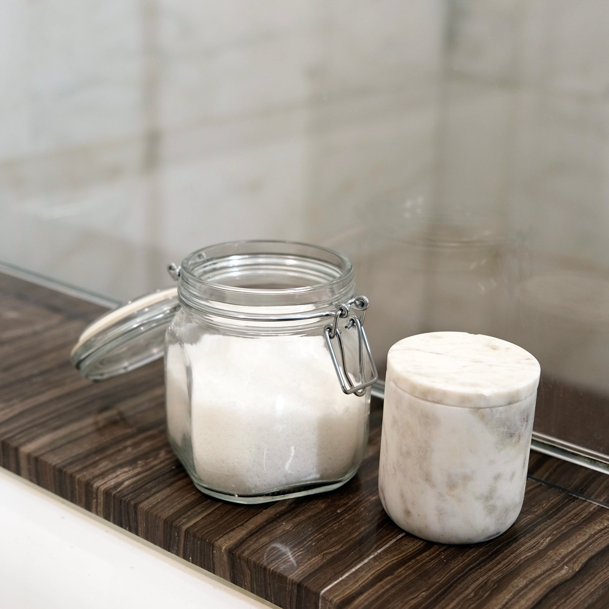 Glass jar with a marble lid on a wooden surface next to a marble container.
