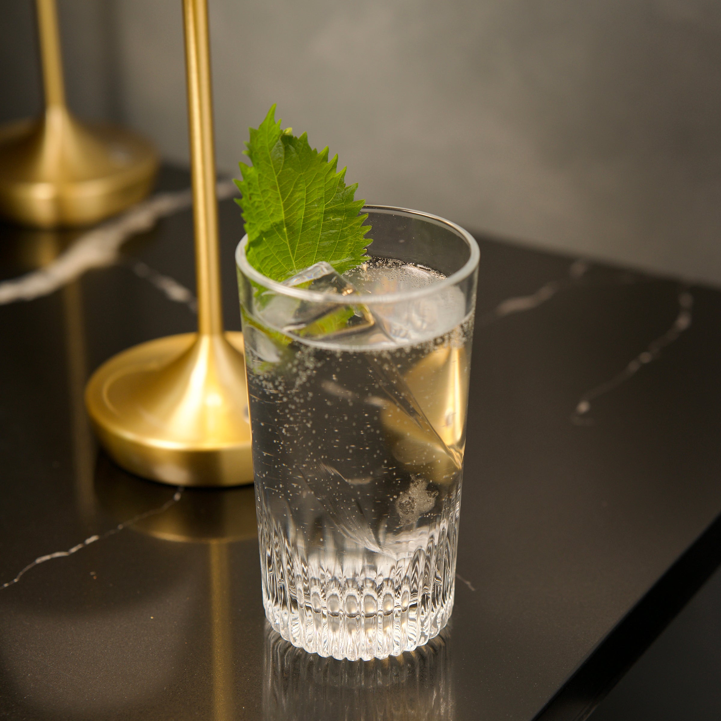 Clear Graphics Beverage glass with a cocktail and leaf on a dark surface with gold accents