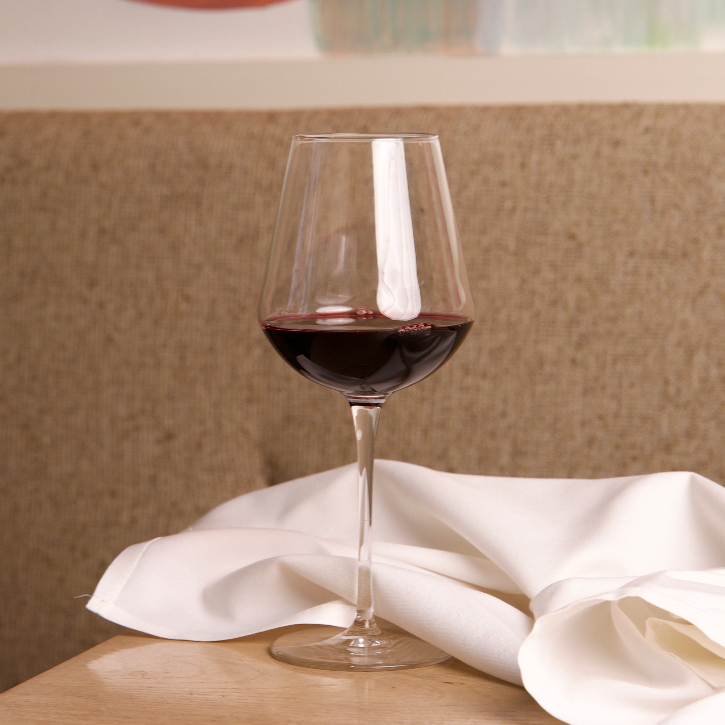 InAlto Uno large glass filled with red wine on a wooden table with a white cloth, blurred background