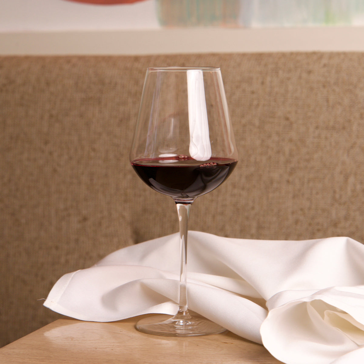 InAlto Uno large glass filled with red wine on a wooden table with a white cloth, blurred background