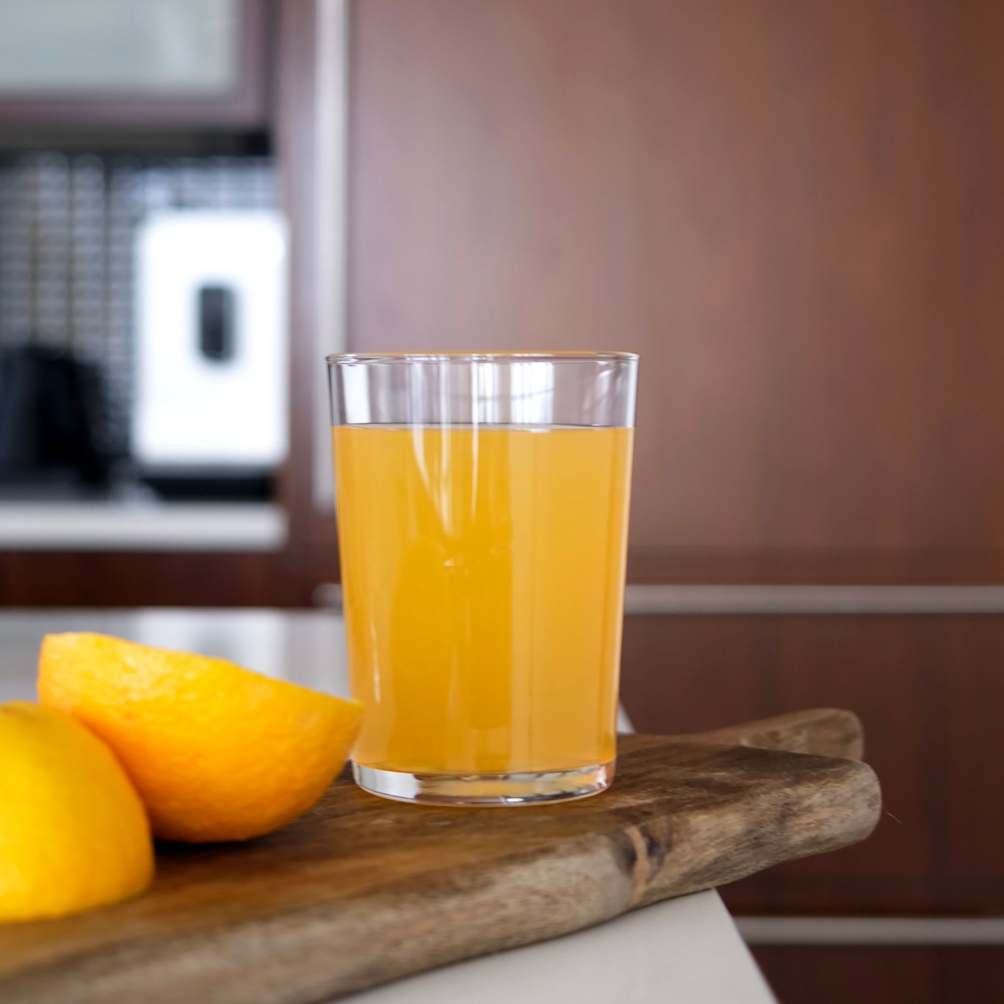 Glass of orange juice on a wooden cutting board with lemons in a kitchen setting