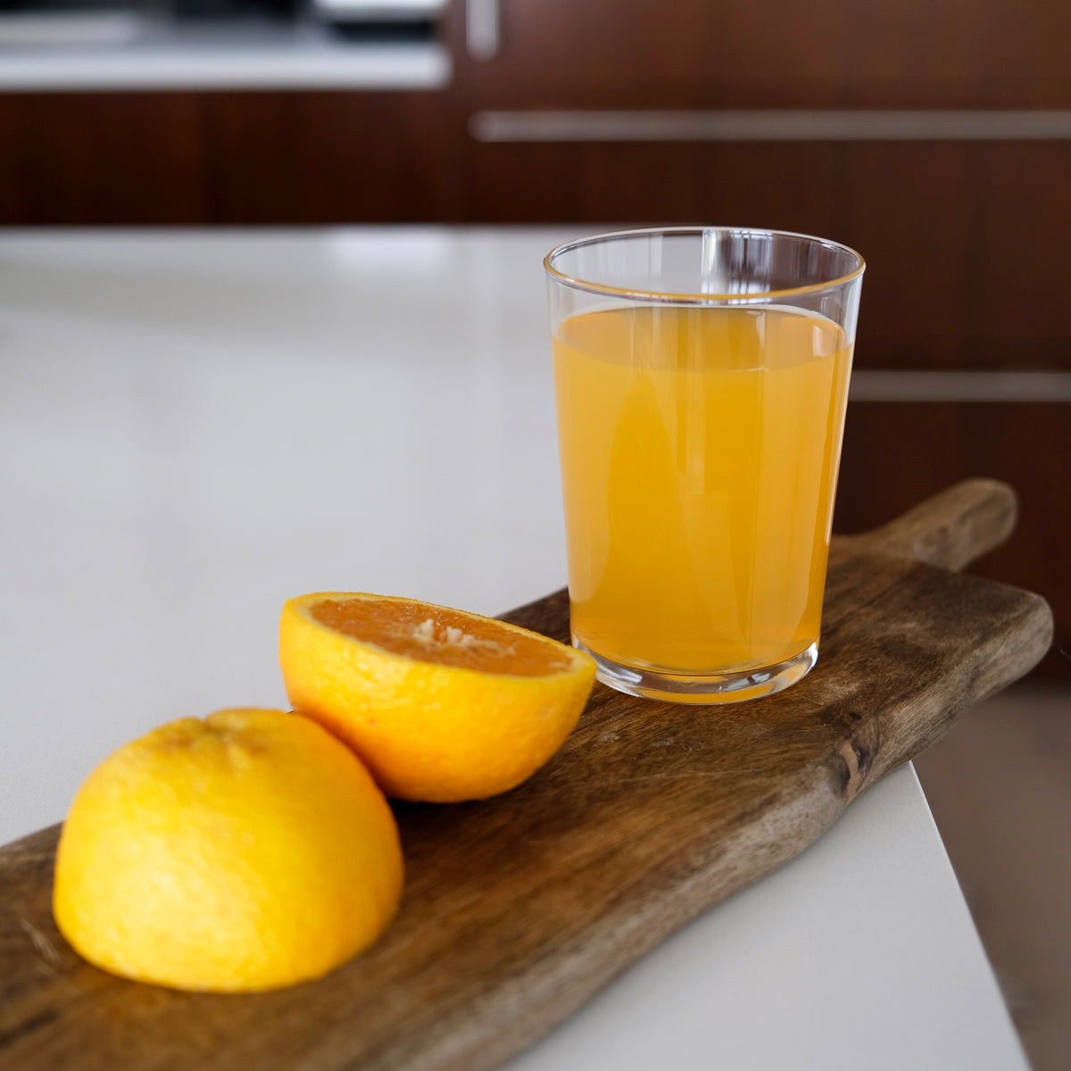 Glass of orange juice on a wooden cutting board with two oranges in a kitchen setting