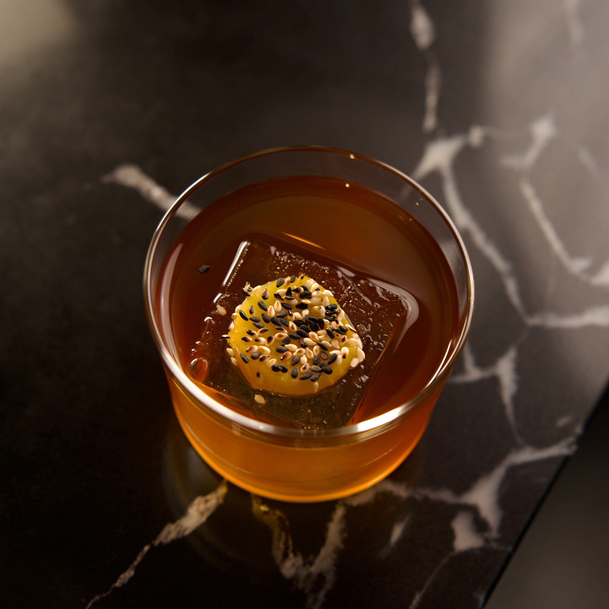 Swirl Rum glass filled with amber-colored cocktail with a spherical garnish on a dark marble surface