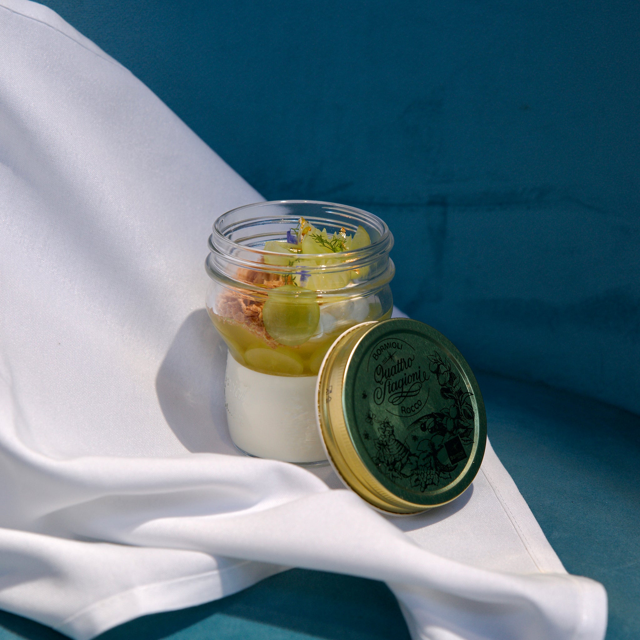 Jar of dessert with a green lid on a white surface with a blue background
